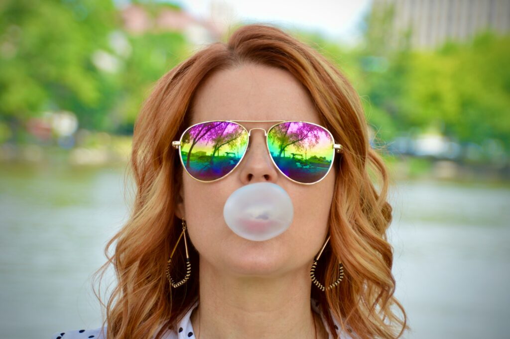 a woman wearing sunglasses blowing a bubble